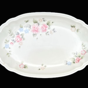 May include: An oval serving platter with a scalloped edge. The white ceramic dish is decorated with pink, blue, and light green floral patterns. The flowers are clustered in several areas around the rim of the platter.