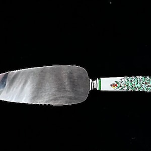 May include: A silver cake server with a white handle decorated with a green and red Christmas tree design.