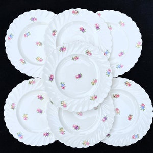 May include: Set of six white ceramic dinner plates with a scalloped edge and a delicate floral pattern in shades of pink, blue, and yellow.