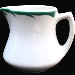 May include: White ceramic creamer with a green rim and a green line design.