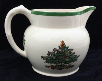 May include: White ceramic pitcher with a green rim and a Christmas tree design. The tree is decorated with ornaments, lights, and a figure at the top.