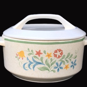 May include: A white ceramic casserole dish with a floral design in shades of yellow, orange, red, blue, and green. The dish has a lid with a handle.