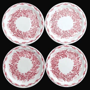 May include: Four white ceramic plates with a red floral rose pattern. Each plate features a central white area surrounded by a wreath of roses and a decorative border. The plates are arranged on a black background.