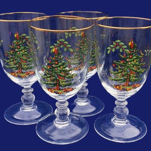May include: Set of four clear wine glasses with gold rims. Each glass features a detailed Christmas tree design with colorful ornaments and gifts at the base. The glasses have a classic stem and base.