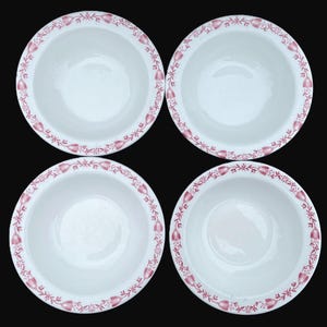 May include: Four white ceramic bowls with a red floral border. The bowls are round with a simple design. The floral border is a repeating pattern of stylized flowers and leaves. The bowls are arranged in a square on a black background.
