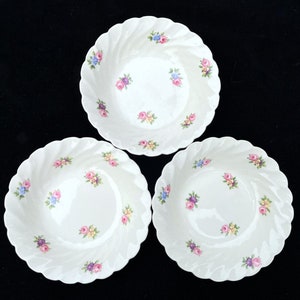 May include: Three white ceramic bowls with a scalloped edge and a floral pattern. The bowls have a white background with pink, blue, and yellow flowers.