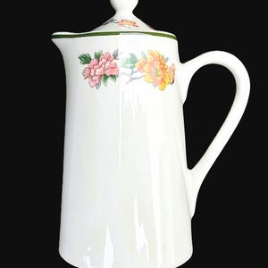 May include: White ceramic coffee pot with a lid and handle. The pot is decorated with pink and yellow floral designs. The rim of the lid has a green border. The pot is tall and slender.