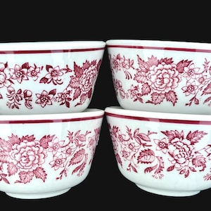 May include: Four white ceramic bowls with a red floral pattern. Each bowl has a red rim and is decorated with a detailed design of flowers and leaves. The bowls are stacked in two pairs.