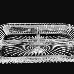 May include: A clear, rectangular divided serving dish with a starburst design in the center. The dish has a ribbed border and is made of glass. The dish is designed to hold multiple items.