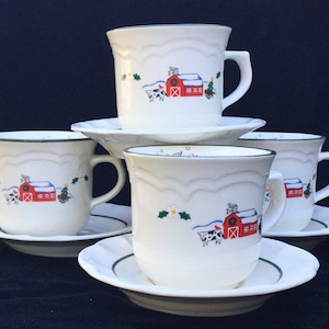 May include: Set of four white ceramic teacups and saucers with a green rim. Each cup and saucer features a winter scene with a red barn, a cow, and a Christmas tree.