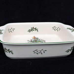 May include: Rectangular white ceramic baking dish with green trim and handles. Decorated with green holly and red berry sprigs, and a Christmas tree scene. A festive serving piece for holiday meals.