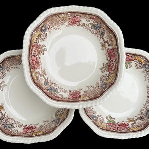 May include: Three cream-colored ceramic bowls with a scalloped edge and a brown, pink, and yellow floral border pattern. The design features intricate botanical illustrations and scrollwork around the rim, surrounding a plain white center.