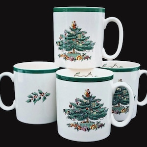 May include: Set of four white ceramic mugs with green trim. Each mug features a different Christmas tree design. One mug has a holly sprig design.