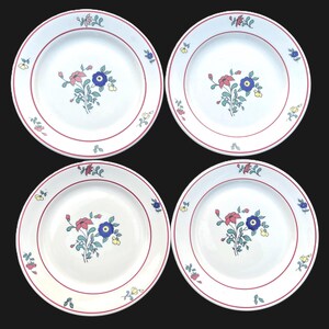 May include: A set of four white ceramic dinner plates, each featuring a central floral motif with pink, blue, and yellow flowers and green leaves. The rim of each plate is decorated with a thin red circular line and small floral accents.