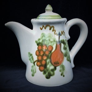 May include: White ceramic teapot with a green and brown floral design featuring a pear and grapes. The teapot has a lid and a handle.