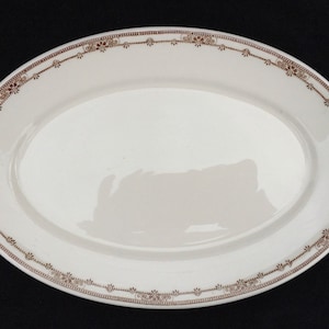 May include: White oval serving platter with a brown decorative border. The border is a repeating pattern of small flowers and dots.