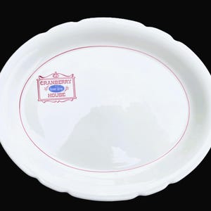 May include: White oval serving platter with a scalloped edge and a red border. The platter features the text "CRANBERRY HOUSE Ocean Spray" in a rectangular frame.