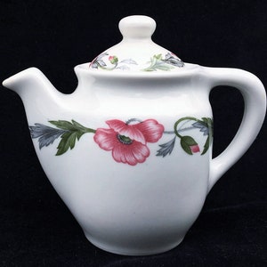 May include: White ceramic teapot with a floral design featuring pink poppies and green leaves. The teapot has a lid and a handle.