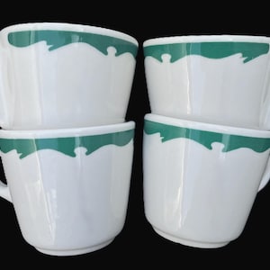 May include: Four white ceramic coffee cups with a green scalloped design around the rim. Each cup has a rounded handle. The cups are stacked in pairs against a black background.
