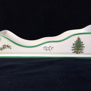 May include: A white ceramic Christmas sleigh with a green trim and a festive Christmas tree design. The sleigh is perfect for holding holiday treats or small gifts.
