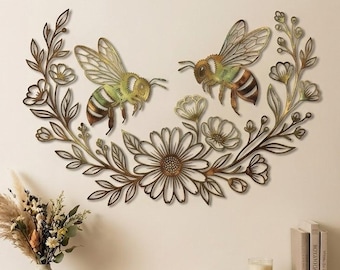Puede incluir: Una pieza de arte mural de metal que presenta dos abejas rodeadas por un arreglo curvo de flores y hojas. El diseño tiene un acabado en tonos dorados y bronce metálicos, mostrando detalles intrincados de pétalos, follaje y alas de abeja.