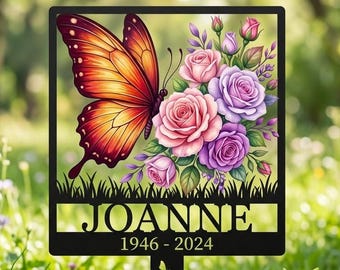 Puede incluir: Un estaca de jardín conmemorativa de metal negro con una mariposa grande de color naranja y rojo junto a un ramo de rosas rosas y moradas. El nombre JOANNE y los años 1946-2024 están recortados en el centro. El tallo incluye pequeños recortes de flores.