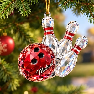 May include: A faceted crystal Christmas ornament featuring a red bowling ball with the name Michael printed in white script and three clear crystal bowling pins with red stripes, all suspended by a gold cord for hanging on a tree branch.