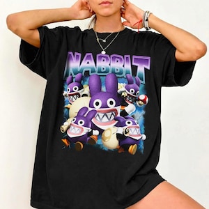 May include: Black t-shirt featuring a graphic of purple cartoon rabbits with sharp teeth and the word "NABBIT" in a purple and blue gradient font. The rabbits have white bellies and orange feet. The background has blue lightning.