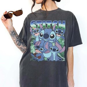 May include: Dark gray t-shirt featuring the word "STITCH" in blue and green, with a graphic of the character Stitch and his friends. The shirt has a vintage, worn look.