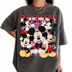 Puede incluir: Camiseta gris con un dise&ntilde;o de Mickey Mouse en varias poses. La palabra "MICKEY" est&aacute; impresa en rojo y rosa en la parte superior. Mickey lleva pantalones cortos rojos y zapatos amarillos. Una prenda casual.