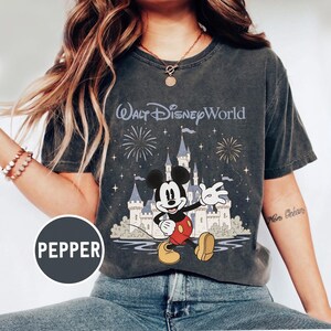 May include: Dark gray t-shirt featuring Mickey Mouse in front of Cinderella's castle with fireworks and the text "Walt Disney World". Mickey is wearing red shorts and yellow shoes. The shirt has a vintage, distressed look.