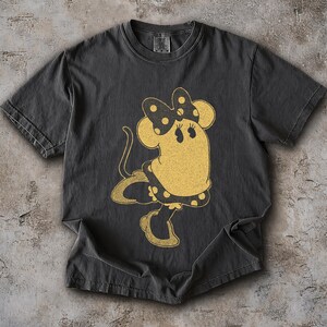 Pode incluir: Camiseta cinza escuro com uma ilustra&ccedil;&atilde;o de rato de desenho animado em estilo vintage. O rato &eacute; amarelo com um la&ccedil;o e um vestido de bolinhas pretas. O gr&aacute;fico tem uma apar&ecirc;ncia envelhecida, dando-lhe uma est&eacute;tica retr&ocirc;.