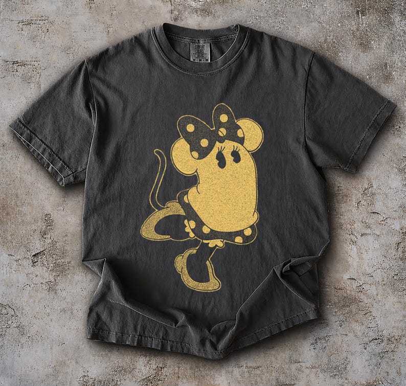 Pode incluir: Camiseta cinza escuro com uma ilustra&ccedil;&atilde;o de rato de desenho animado em estilo vintage. O rato &eacute; amarelo com um la&ccedil;o e um vestido de bolinhas pretas. O gr&aacute;fico tem uma apar&ecirc;ncia envelhecida, dando-lhe uma est&eacute;tica retr&ocirc;.