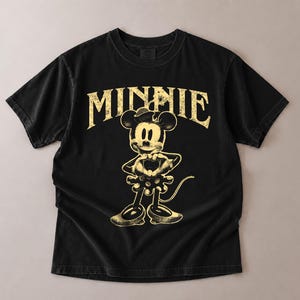 May include: Black t-shirt featuring a distressed graphic of Minnie Mouse with the word "MINNIE" in a vintage font. The design is in a faded yellow color, creating a retro aesthetic. The shirt has short sleeves and a crew neck.