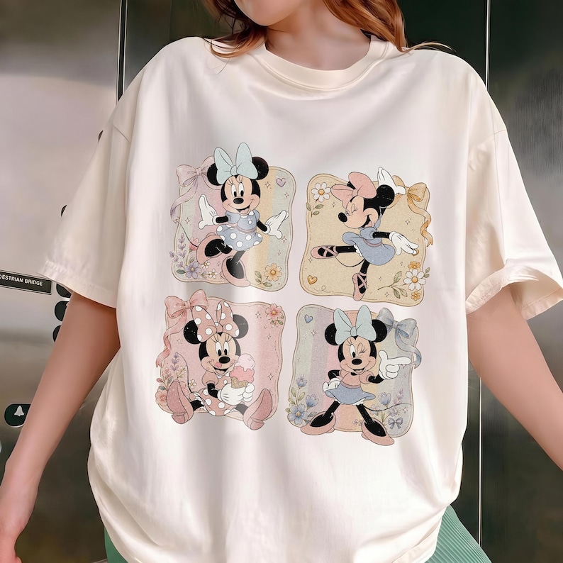May include: Cream-colored t-shirt featuring four square illustrations of Minnie Mouse in various poses. Each illustration has a different background color and floral accents. Minnie Mouse is wearing different outfits and bows in each illustration.