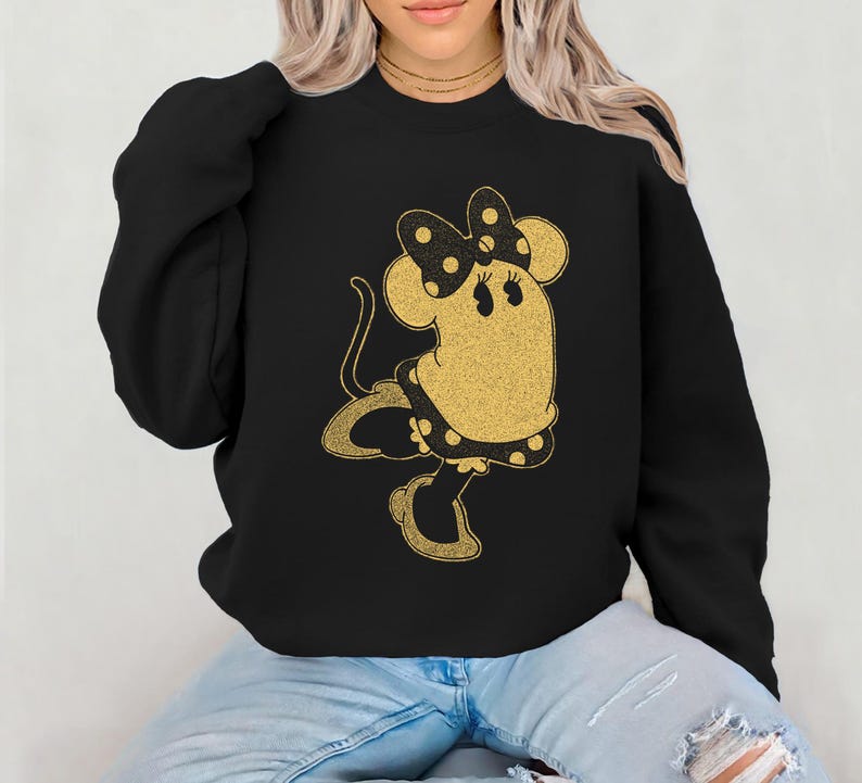 Pode incluir: Camisola preta com um design dourado brilhante de um rato de desenho animado com la&ccedil;o, vestido e sapatos. O rato tem uma cauda longa e est&aacute; em pose de dan&ccedil;a. A camisola &eacute; de estilo casual.