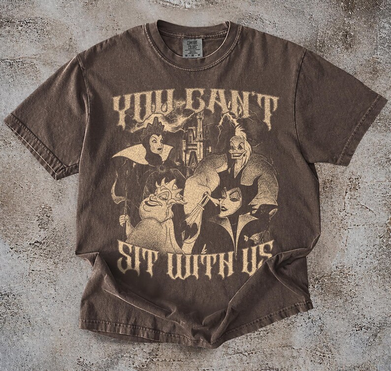 May include: Brown t-shirt featuring a graphic of Disney villains with the text "YOU CAN'T SIT WITH US". The design includes characters like Maleficent and the Evil Queen. The shirt has a vintage, distressed look.