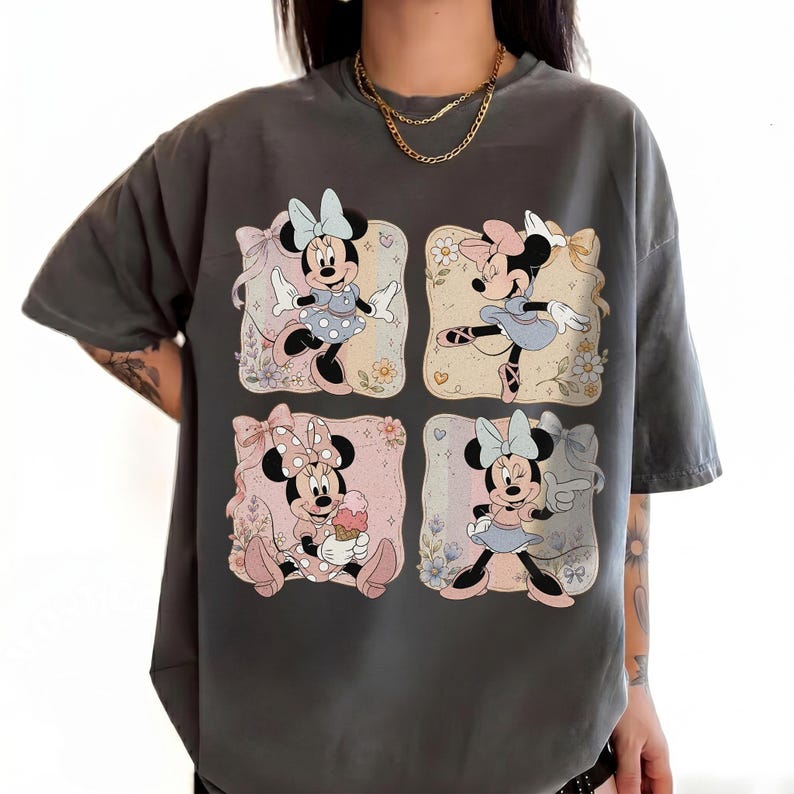 May include: Dark gray t-shirt featuring four squares with Minnie Mouse illustrations. Each square shows Minnie in different poses, wearing dresses and bows, with floral and pastel backgrounds. The shirt is a casual, oversized style.