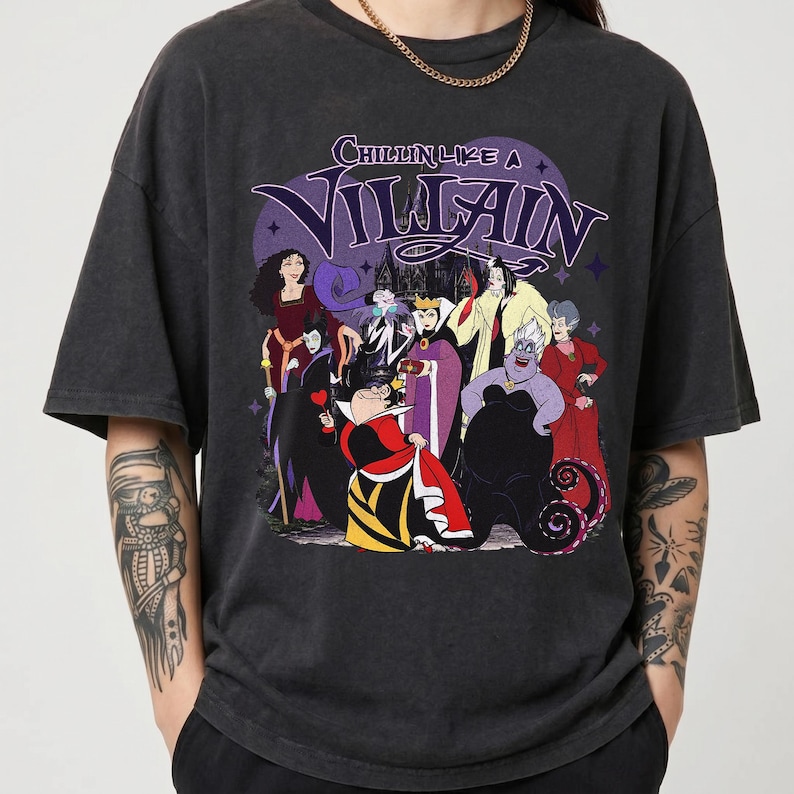 K&ouml;nnte beinhalten: Ein anthrazitfarbenes Kurzarm-T-Shirt mit einem Grafikdruck verschiedener animierter B&ouml;sewichte. Der Text "CHILLIN LIKE A VILLAIN" ist in Lila &uuml;ber den Charakteren aufgedruckt, die Outfits in Rot, Schwarz, Lila und Gelb tragen.