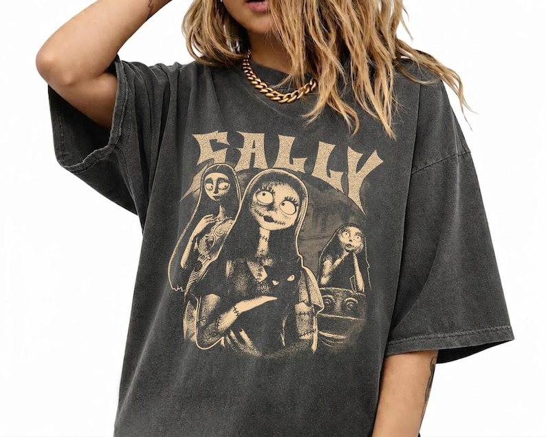 May include: A charcoal gray oversized t-shirt featuring a distressed beige graphic print of the character Sally from The Nightmare Before Christmas. The design includes the text SALLY in a stylized font above three depictions of the character.