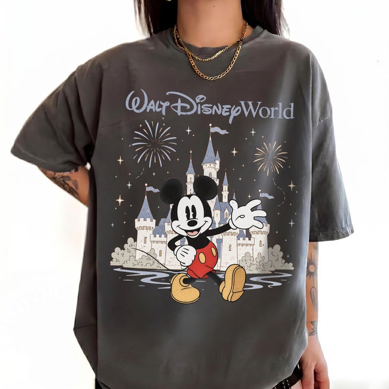 May include: Dark gray t-shirt featuring Mickey Mouse in front of Cinderella's castle with fireworks and the text "Walt Disney World". Mickey is wearing red shorts, yellow shoes, and white gloves. The shirt has a vintage, worn look.