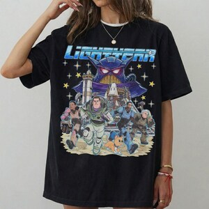 May include: Black t-shirt featuring a graphic from the movie Lightyear. The design includes the title "Lightyear" in blue, a purple villain, and several characters running across a sandy landscape with stars.