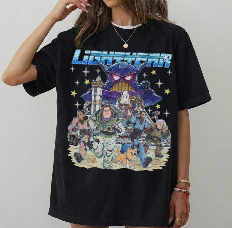 May include: Black t-shirt featuring a graphic from the movie Lightyear. The design includes the title "Lightyear" in blue, a purple villain, and several characters running across a sandy landscape with stars.