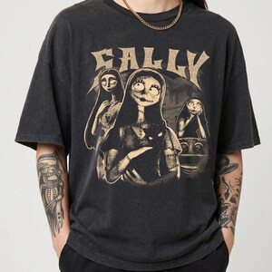 May include: A charcoal gray short-sleeve t-shirt featuring a graphic print of the character Sally from The Nightmare Before Christmas. The design includes the text SALLY in a stylized font above three illustrations of the character in various poses.
