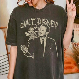 May include: Dark gray t-shirt featuring a vintage-style graphic of Walt Disney with Mickey Mouse and the text "Walt Disney". The shirt has a classic crew neck and short sleeves.