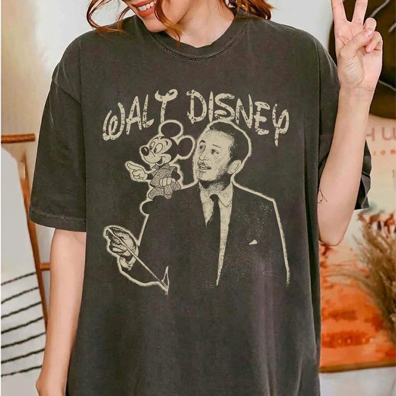 May include: Dark gray t-shirt featuring a vintage-style graphic of Walt Disney with Mickey Mouse and the text "Walt Disney". The shirt has a classic crew neck and short sleeves.