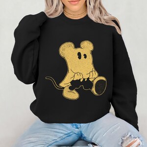 May include: Black sweatshirt featuring a gold-colored cartoon mouse ghost design. The mouse ghost has large ears, a tail, and is sitting down. The sweatshirt is a long-sleeved crew neck.