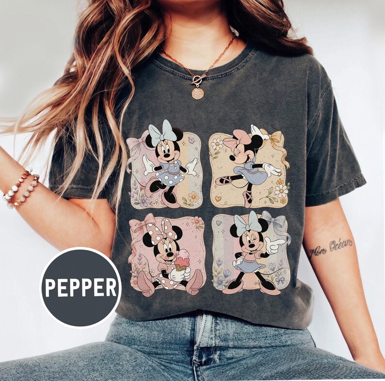 May include: Dark gray t-shirt featuring a four-panel design of Minnie Mouse in various poses. Each panel has a different pastel background with floral accents. Minnie is wearing different outfits and bows in each panel. The word "PEPPER" is printed on a circular label.