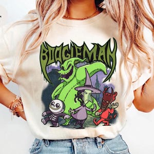 Könnte beinhalten: Elfenbeinfarbenes T-Shirt mit einer Grafik des Boogieman und anderer Charaktere aus einem beliebten Animationsfilm. Das Design enthält das Wort "Boogieman" in Grün, mit Charakteren in Grün, Lila, Rot und Schwarz.