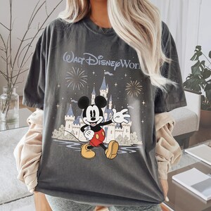May include: Dark gray t-shirt featuring Mickey Mouse in front of a castle with fireworks and the text "Walt Disney World". Mickey is wearing red shorts and yellow shoes. The shirt has a vintage look.